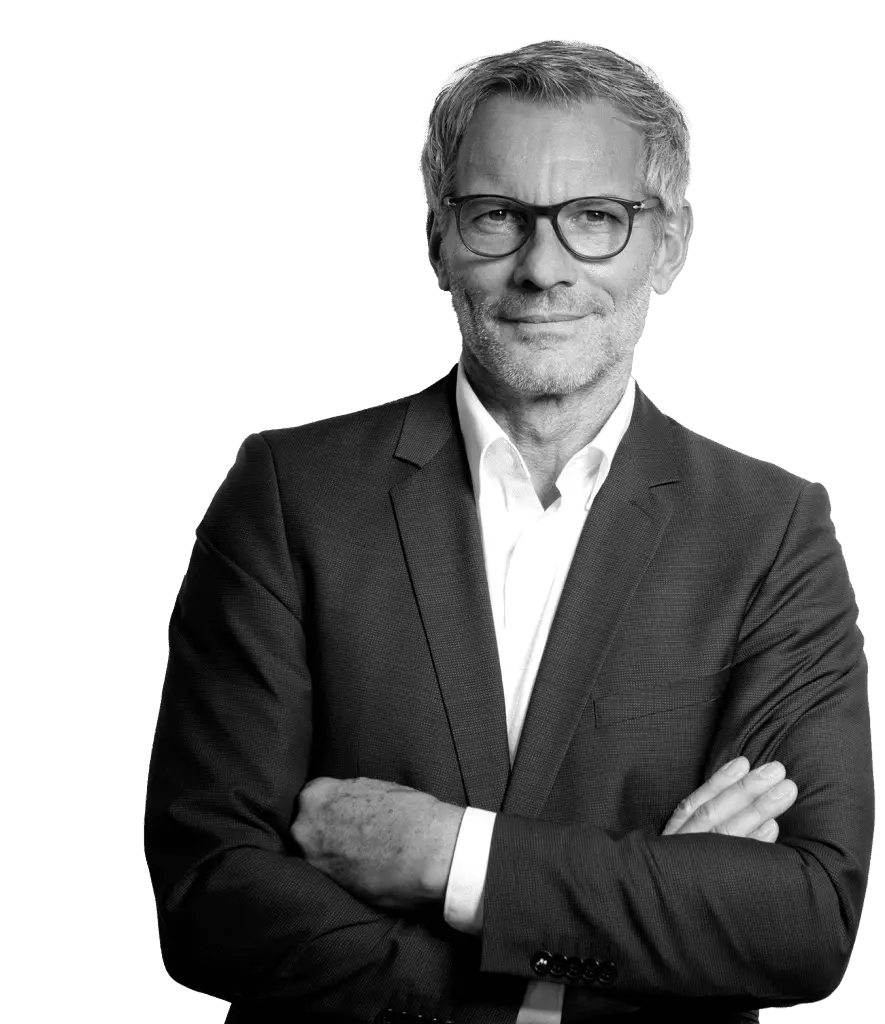 Man with grey hair and glasses in a dark suit standing with his arms crossed